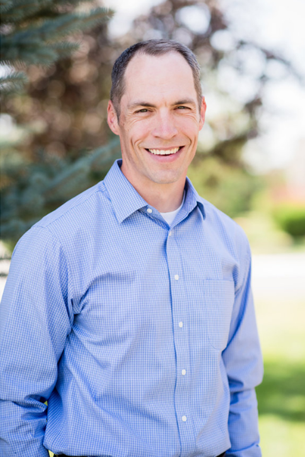 portrait of Dr. Liljenquist, white man smiling broadly wearing light blue shirt, standing outside